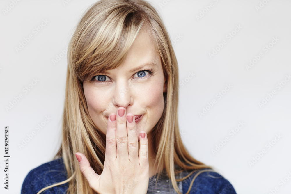Blue eyed blond woman covering mouth, portrait Blue eyed blond woman covering mouth, portrait