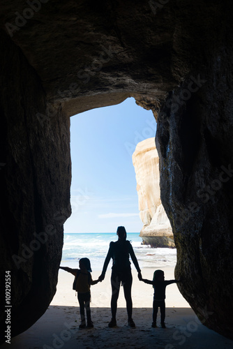 Silhouette of mother with two kids in a cave at Tunnel beach near Dunedin, New Zealand