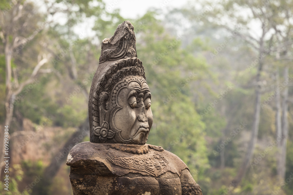 Guardian statue in South Gate of Angkor Thom temple, Cambodia. Trees background