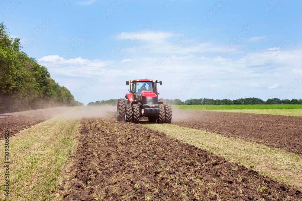 Obraz premium Modern tech red tractor plowing a green agricultural field in spring on the farm. Harvester sowing wheat.