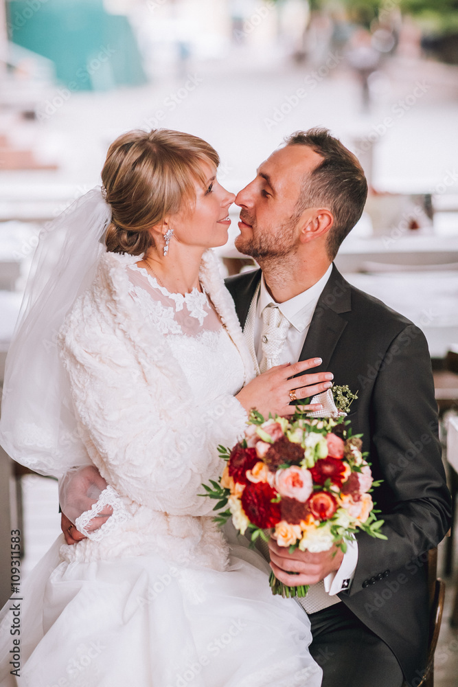 Happy smiling newlywed couple sitting and kissing on terrace with bouquet Happy smiling newlywed couple sitting and kissing on terrace with bouquet