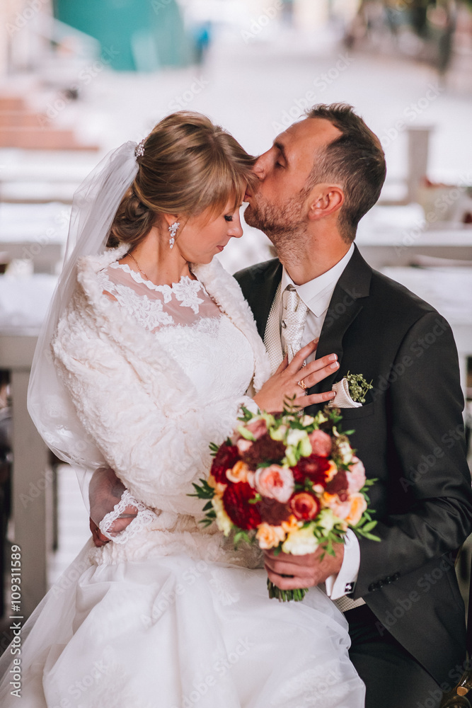 Happy smiling newlywed couple sitting and kissing on terrace with bouquet Happy smiling newlywed couple sitting and kissing on terrace with bouquet
