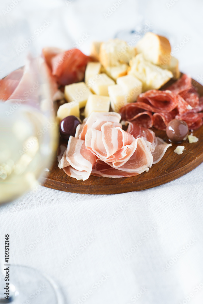 Traditional italian apero: white wine and plate with  prosciutto crudo, salami, parmesan cheese, olives and bread. Selective focus.