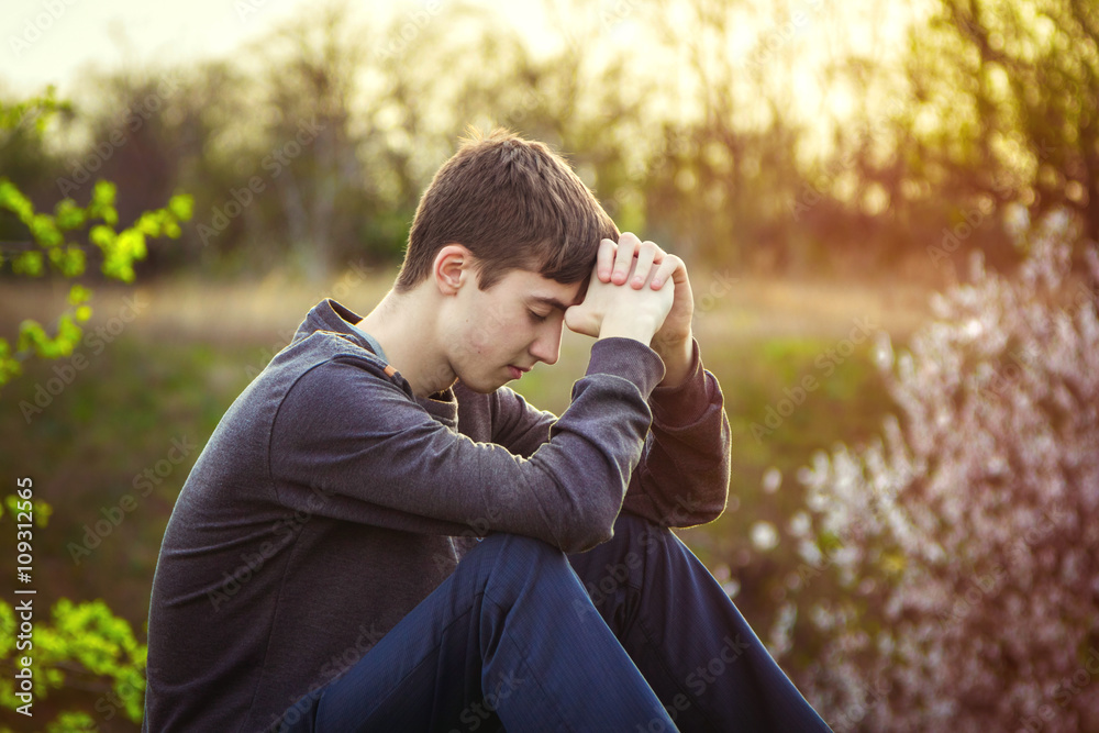 Sad guy sitting alone on the ground with his eyes closed in sunset light, outdoors Sad guy sitting alone on the ground with his eyes closed in sunset light, outdoors