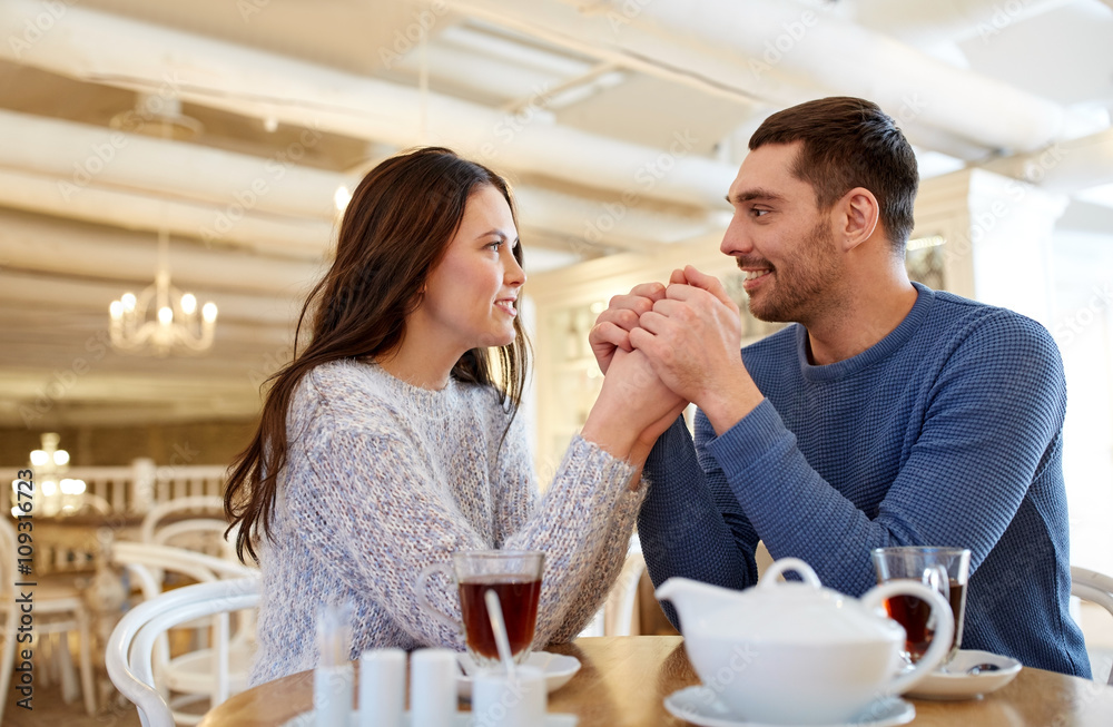 happy couple with tea holding hands at restaurant
