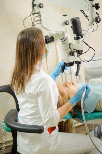 Obraz na plátne Female dentist doctor treating root canals using microscope at dentistry office