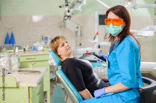 Female dentist is holding dentist photopolymer lamp getting ready to treat patient in clinic. Doctor is wearing gloves and glasses. Stomatology equipment.