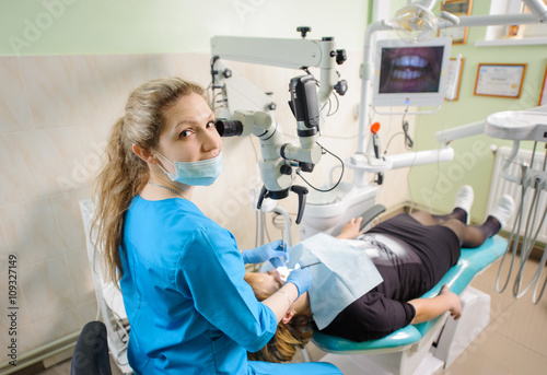 Female doctor working with microscope at modern dentist clinic. Teeth care and tooth health. Dentist checking patient teeth through the microscope and looking to the camera