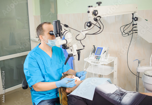Male dentist working with microscope at modern dentist clinic. Teeth care and tooth health. Dentist checking patient teeth looking in dental mirror through the microscope.