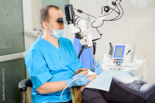 Male dentist working with microscope at modern dentist office. Teeth care and tooth health. Doctor treating root canals through the microscope. Stomatology equipment