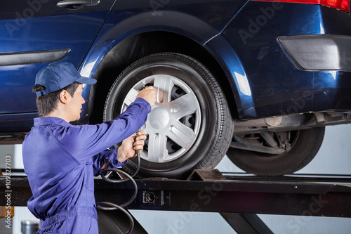 Repairman Inflating Tire Of Lifted Car