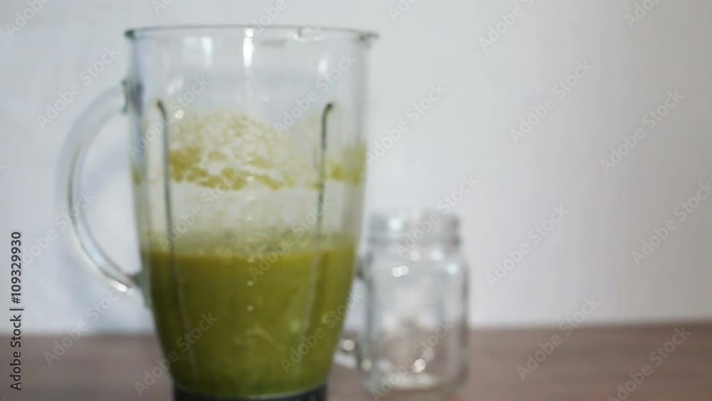 A blender jar with green healthy smoothie and a mason jar on a wooden table. Slow motion A blender jar with green healthy smoothie and a mason jar on a wooden table. Slow motion