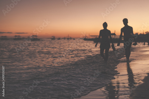 Traditional philippine boats floating in the sea and silhouettes of a woman and man walking along the sea shore during sunset. Panglao Island, Philippines.