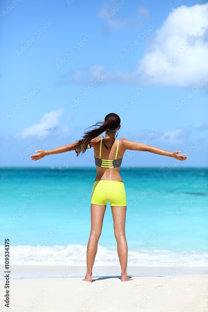 Happy running woman winning - fitness goal concept on beach. Young Asian female runner serene and blissful cheering with arms up, wearing wireless bluetooth earphones and smart phone armband. Happy running woman winning - fitness goal concept on beach. Young Asian female runner serene and blissful cheering with arms up, wearing wireless bluetooth earphones and smart phone armband.