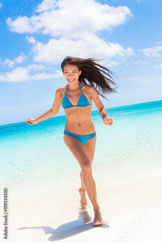 Beach sexy bikini Asian woman having fun coming out of water running laughing playful relaxing on tropical getaway paradise. Young ethnic model with slim weight loss beach body. Summer vacation travel