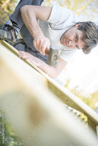 Low angle view of young man using a hammer or mallet to nail a n