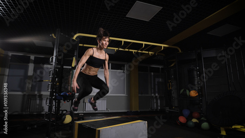 young female athlete doing a box jump at the gym - focus on the woman