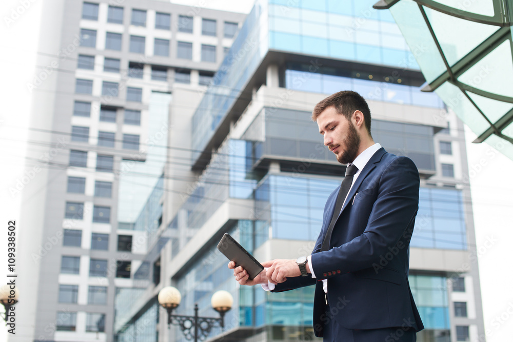 Businessman holding tablet on background of buildings with glass facades