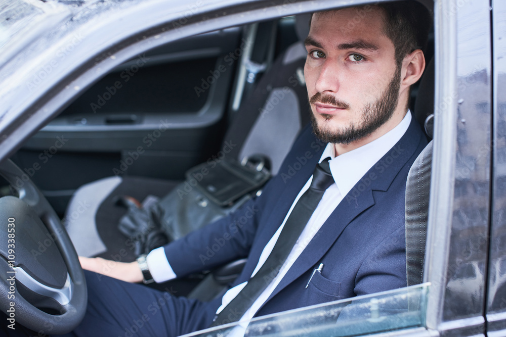 The portrait of the guy in the suit sitting behind the wheel of a car