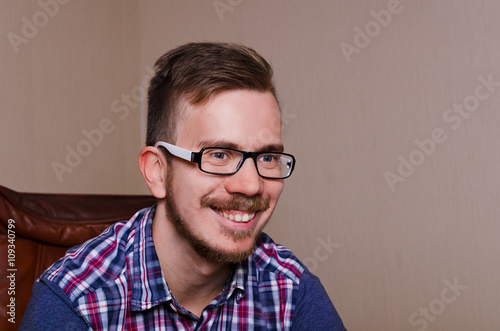 Happy funny guy sit ob chair and smile. Hipster with glasses asn beard have happy emotion.