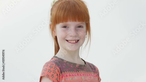 Little ginger girl closes and openes eyes, smiling, white background, close up photo