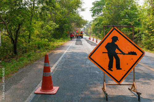 Construction sign on country road with trees on roadside background - Roadworks Ahead. Orange Sign 