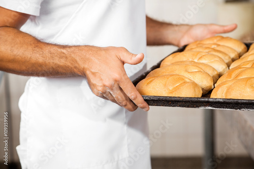 Midsection Of Male Baker Carrying Breads In Baking Tray