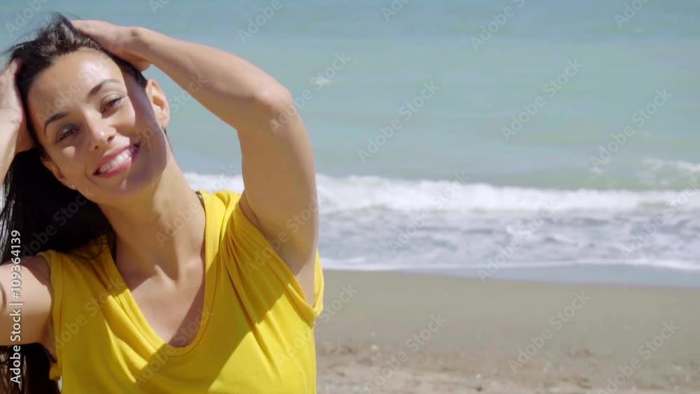 Happy vivacious young woman enjoying nature standing with her hands to her long hair in the breeze off the ocean on a tropical beach head and shoulders. Happy vivacious young woman enjoying nature standing with her hands to her long hair in the breeze off the ocean on a tropical beach head and shoulders.