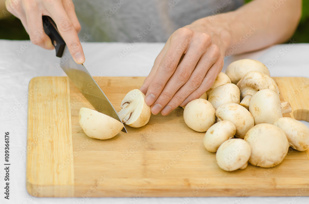 Mushrooms and Food theme: man preparing porcini mushrooms on a wooden board on a background of green grass in summer Mushrooms and Food theme: man preparing porcini mushrooms on a wooden board on a background of green grass in summer