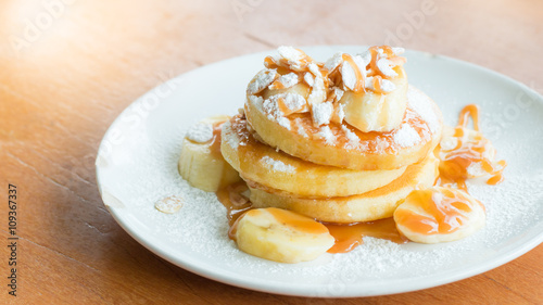 Bannana pancake toping with icing sugar,banana,caramel and almond on wooden table,lighting from behide.