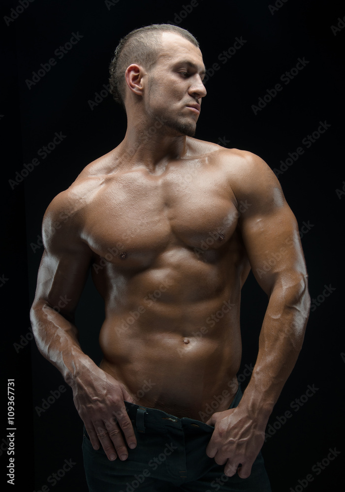 Bodybuilder and strip theme: beautiful with pumped muscles naked man posing in the studio on a dark background Bodybuilder and strip theme: beautiful with pumped muscles naked man posing in the studio on a dark background