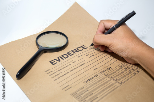 hand with pen writing on evidence paper with magnifying glass
