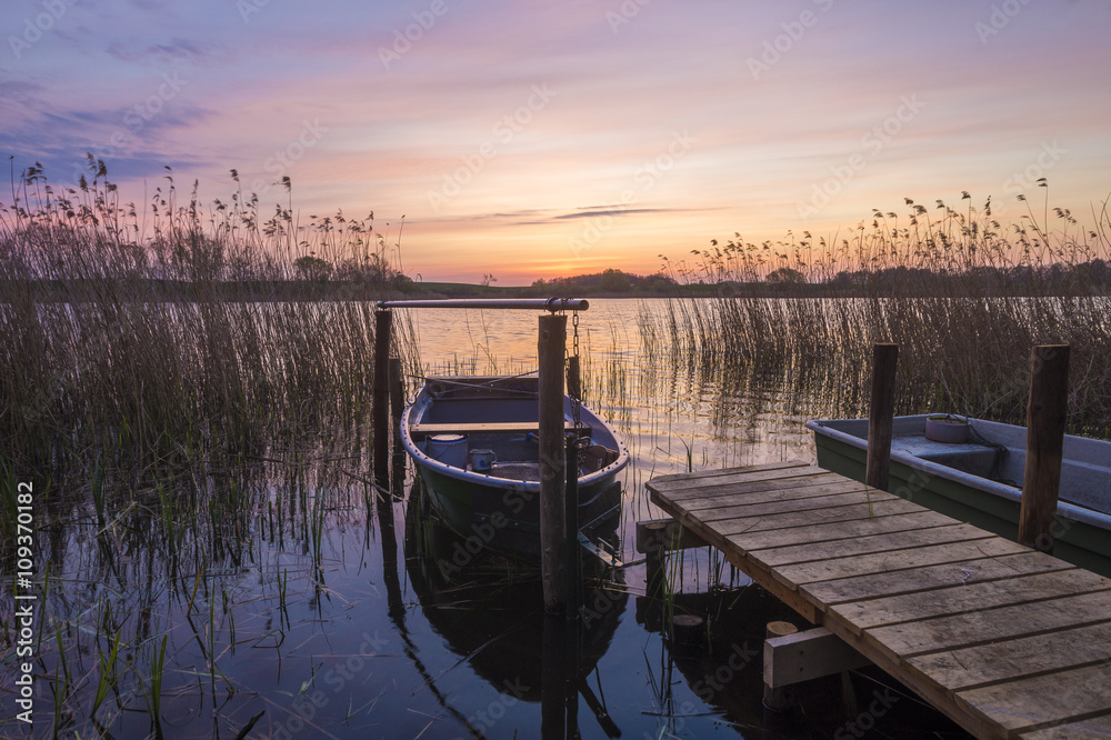 Fotografie łódka zacumowana do drewnianego pomostu nad jeziorem