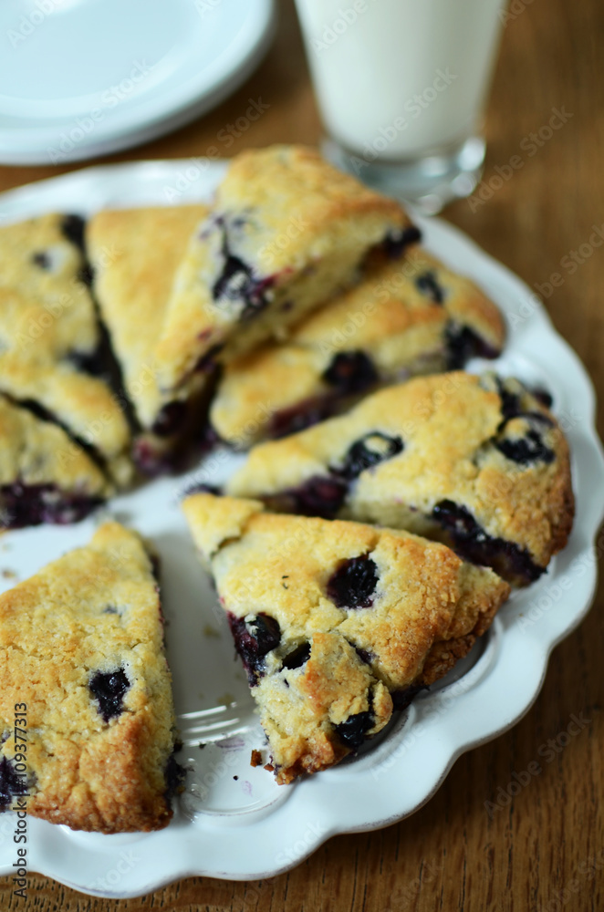 Blueberry scones cut in triangles on white plate with a glass of milk