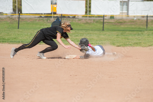 Black uniform softball player tagging the player sliding in white.