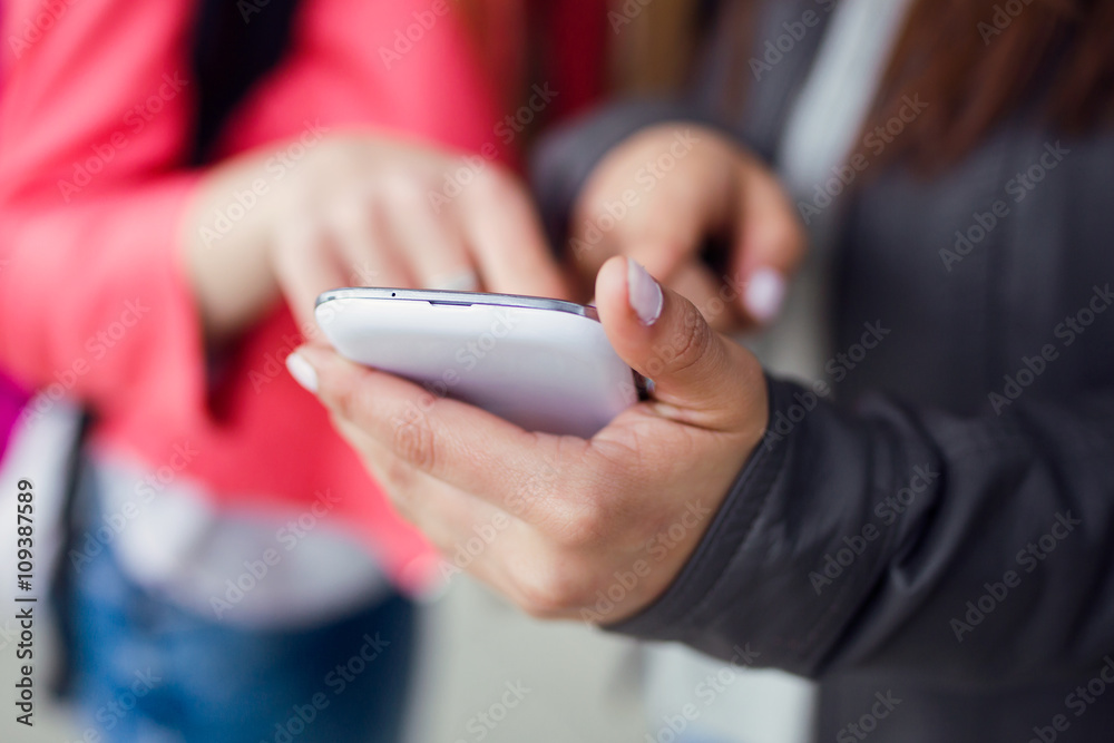 Two beautiful students using mobile phone in the street. Two beautiful students using mobile phone in the street.