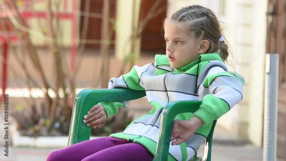 Seven-year girl thoughtfully sitting on a chair and smiling happily seeing something Seven-year girl thoughtfully sitting on a chair and smiling happily seeing something