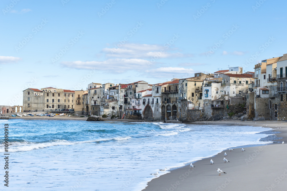 Empty beach of Cefalu leading to its old town in a sunny winter day. Sicily. Italy