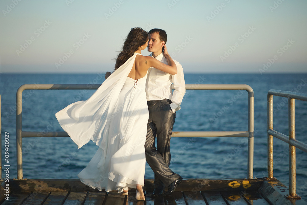 Gorgeous wedding couple kissing on pier under spray, splashes an Gorgeous wedding couple kissing on pier under spray, splashes an