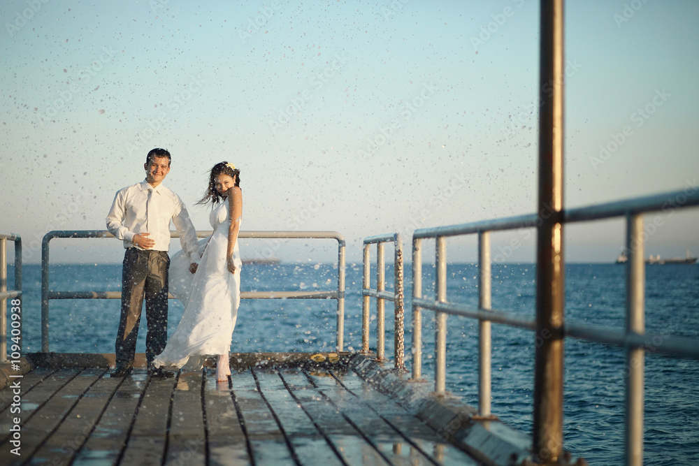 Gorgeous wedding couple walking through pier, splashes and drops Gorgeous wedding couple walking through pier, splashes and drops