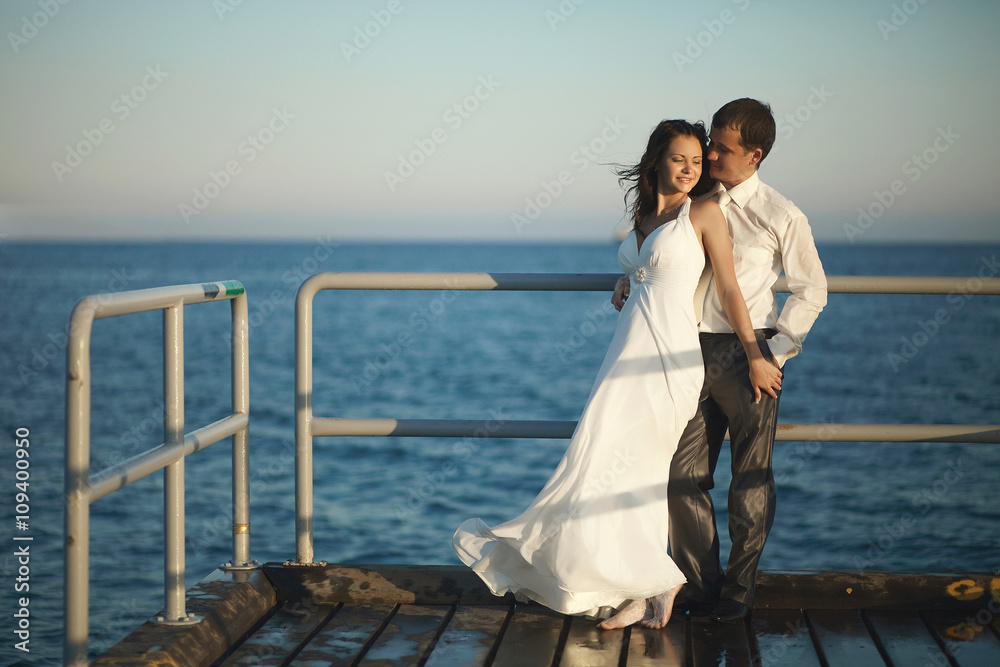 Gorgeous wedding couple standing on pier under spray, splashes a Gorgeous wedding couple standing on pier under spray, splashes a