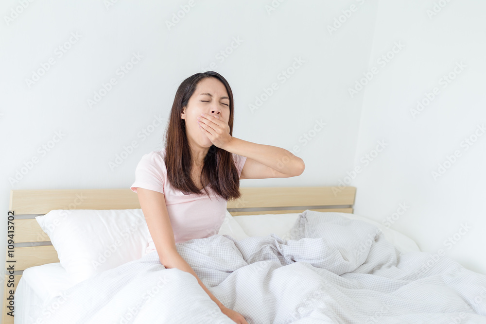 Young woman sitting on the bed and yawning Young woman sitting on the bed and yawning