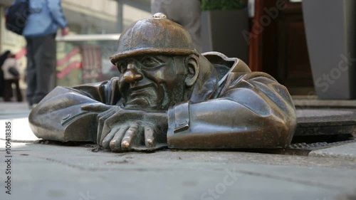 Cumil - statue of man peeking out from under a manhole cove
