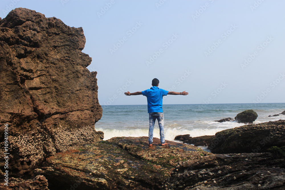 Open arms. A young man standing on a cliff with his arms wide open.