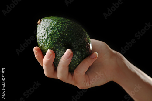 Female hand holding fresh avocado on black background