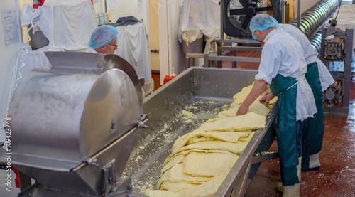 Men processing cheese inside a factory using a mill in which they shred blocks of cheese for packing