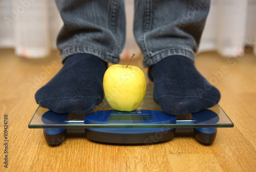 male feet standing on a  scale with green apple beetween them, d photo