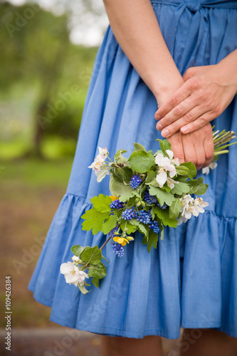 Close-up of woman's hand holding a branch of blooming apple tree. Blues dress as a background.Spring concept.