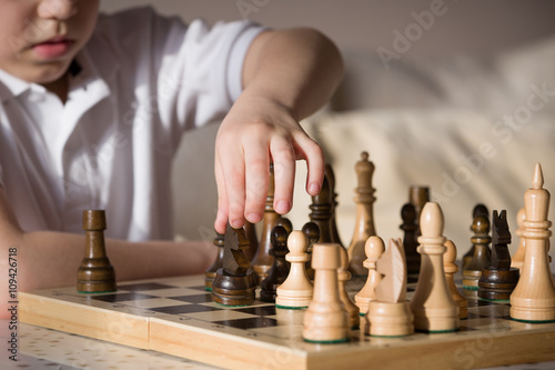 Boy playing chess in the room. Little clever boy concentrated and thinking while playing chess at home.