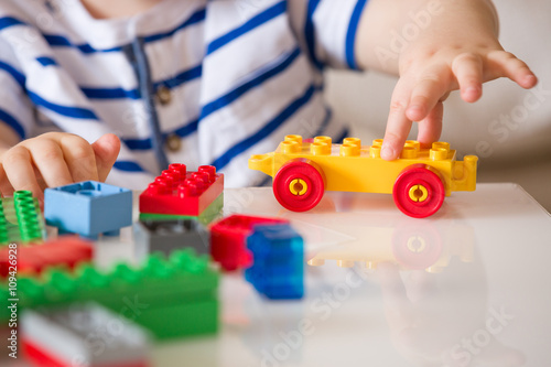 Close up of child's hands playing with colorful plastic bricks at the table. Toddler having fun and building out of bright constructor bricks. Early learning.  stripe background. Developing toys